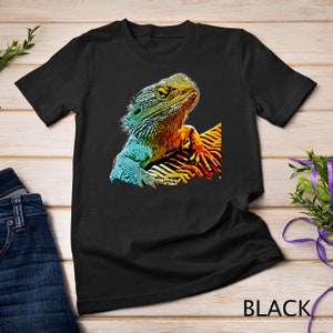 Może przedstawiać: Czarny t-shirt z kolorową grafiką jaszczurki z przodu. Jaszczurka jest w żywych kolorach zielonym, niebieskim i żółtym.