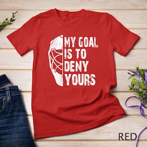 May include: Red t-shirt with a white hockey goalie mask graphic and the text "My goal is to deny yours".