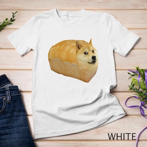 May include: White t-shirt with a printed image of a Shiba Inu dog's head inside a loaf of bread. The dog is looking directly at the viewer.