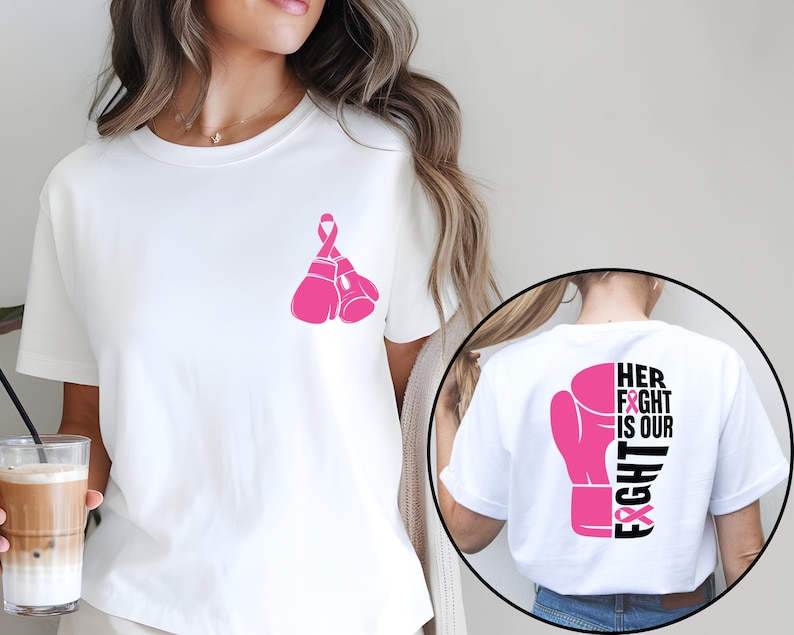 Pode incluir: Camiseta branca com um design de luva de boxe e fita rosa. A frente da camiseta apresenta duas luvas de boxe rosa com uma fita rosa. A parte de tr&aacute;s da camiseta tem uma luva de boxe rosa com o texto "HER FIGHT IS OUR FIGHT".