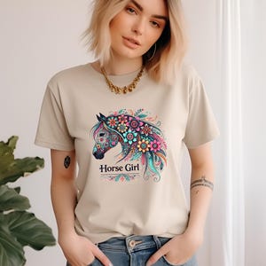 Puede incluir: Una camiseta beige con un dise&ntilde;o de caballo floral colorido y el texto "Horse Girl".