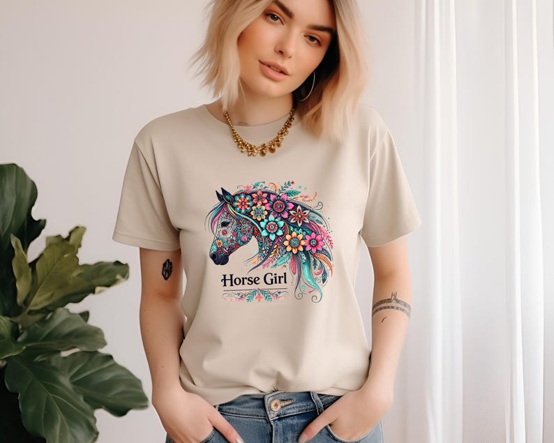 Puede incluir: Una camiseta beige con un dise&ntilde;o de caballo floral colorido y el texto "Horse Girl".