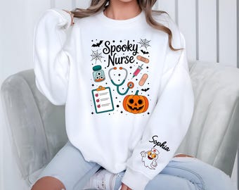 May include: White sweatshirt with a Halloween-themed design. The graphic includes the text "Spooky Nurse" with medical tools, a jack-o'-lantern, bats, and a ghost. The name "Sophia" is printed on the sleeve.