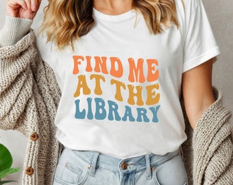 May include: White t-shirt with the text "FIND ME AT THE LIBRARY" in a retro font with orange, yellow, and blue colors.