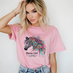 Puede incluir: Una camiseta rosa con un dise&ntilde;o de caballo floral colorido y el texto "Horse Girl".