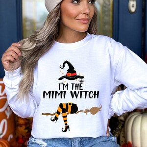 May include: White long-sleeve sweatshirt with a black witch graphic and the text "I'm the Mimi Witch".