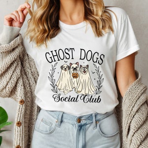 May include: White t-shirt with a graphic of three ghost dogs wearing Halloween costumes. The text "Ghost Dogs Social Club" is printed on the shirt.