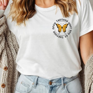 May include: White t-shirt with a black circle graphic featuring a yellow butterfly and the text "Go through what you grow through".