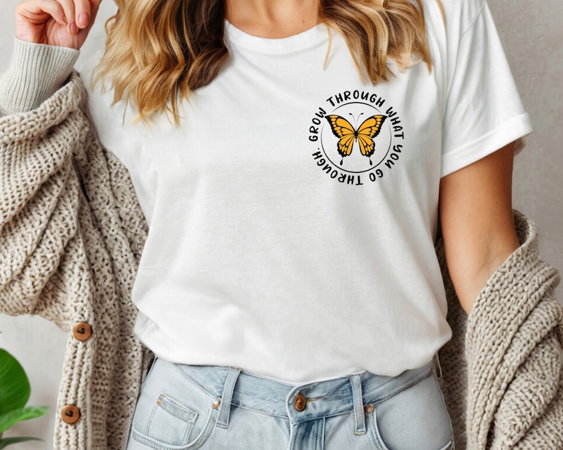May include: White t-shirt with a black circle graphic featuring a yellow butterfly and the text "Go through what you grow through".