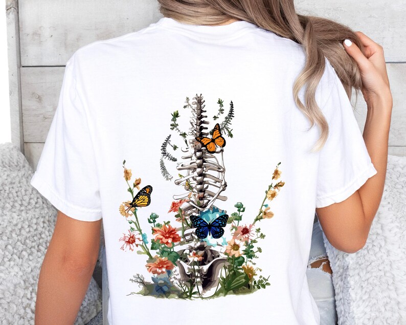 May include: White t-shirt with a graphic of a human spine with flowers and butterflies. The butterflies are orange, blue, and yellow.