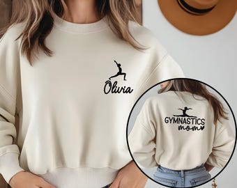 May include: Cream-colored sweatshirt with a black gymnastics silhouette and the name "Olivia" printed on the front. The back of the sweatshirt features a circular image with the words "Gymnastics Mom" and a gymnast silhouette.