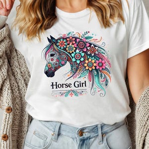Puede incluir: Camiseta blanca con un dise&ntilde;o de caballo floral colorido y el texto "Horse Girl" impreso en la parte delantera.