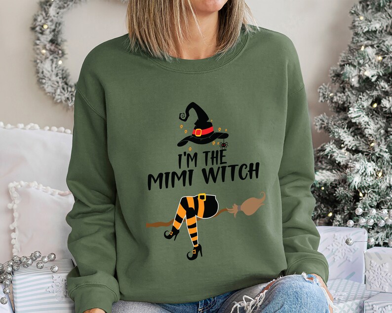 May include: A green sweatshirt with a graphic of a witch on a broomstick. The text on the sweatshirt reads "I'm the Mimi Witch".