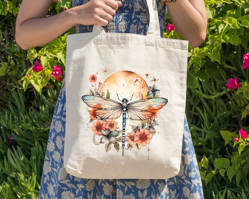 Pu&ograve; includere: Una borsa tote bianca con un design di libellula colorato. La libellula &egrave; circondata da fiori e un cerchio color tramonto. La borsa ha due manici lunghi.