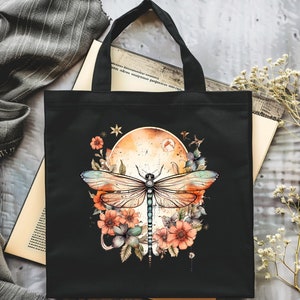 Pu&ograve; includere: Borsa tote nera con un design di libellula e fiori colorati. La libellula ha ali blu, verdi e arancioni. I fiori sono arancioni, rosa e bianchi. Lo sfondo &egrave; una tela nera con una luna in stile acquerello.