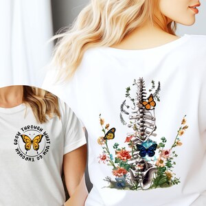 May include: White t-shirt with a graphic of a human spine with flowers and butterflies. The text "Grow through what you go through" is printed on the front of the shirt.