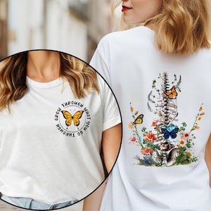 May include: Two white t-shirts with different designs. The first shirt has a butterfly graphic with the text "Grow through what you go through". The second shirt has a butterfly and floral design with a spine graphic.