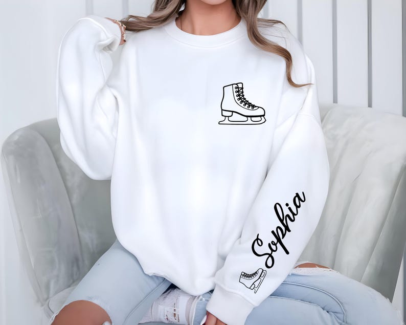 May include: White sweatshirt featuring a black outline of an ice skate on the chest and sleeve. The name "Sophia" is written in cursive on the sleeve. A small ice skate graphic is below the name.