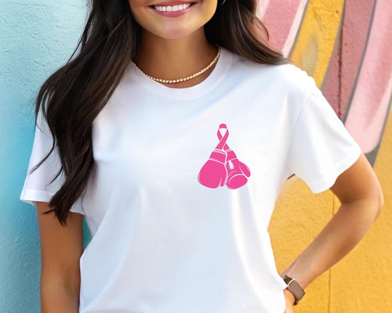 Pode incluir: Camiseta branca com um la&ccedil;o rosa e luvas de boxe, um s&iacute;mbolo de conscientiza&ccedil;&atilde;o sobre o c&acirc;ncer de mama. A camiseta &eacute; feita de um material macio e confort&aacute;vel.