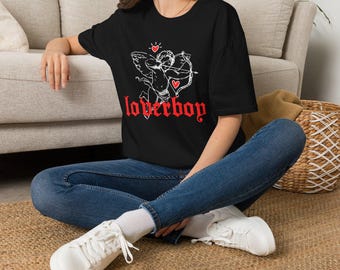 May include: A black short-sleeved t-shirt featuring a white line-art graphic of a winged cupid figure holding a bow and arrow. The design includes two small red hearts and the word "loverboy" printed in a bold, red, gothic-style font.