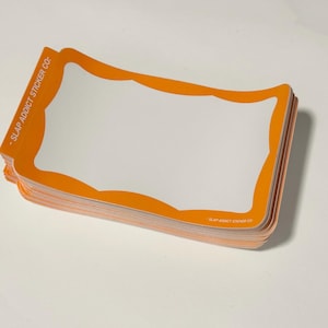 May include: A stack of rectangular stickers with rounded corners, featuring a white center and a thick orange border. The text SLAP ADDICT STICKER CO is printed in white on the orange border along the left side and the bottom right corner.
