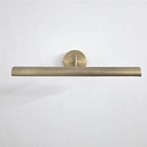 Può includere: Una lampada per quadri color ottone. La lampada ha una barra luminosa cilindrica e una piastra di montaggio circolare. La barra luminosa è orizzontale e montata su una parete bianca. Progettata per illuminare opere d'arte.