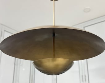 Puede incluir: Una lámpara colgante de oro con una pantalla grande, plana y circular y una pantalla más pequeña, redonda y en forma de cuenco.