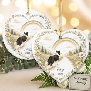 May include: Two heart-shaped ceramic ornaments featuring a black and white Border Collie standing on a path in a meadow with a rainbow, mountains, and floral border. One ornament is personalized with the name Millie and the year 2026, the other with Roxy and 2026.