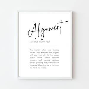 May include: A framed white print featuring the word "Alignment" in black cursive script. The definition below describes aligning choices and values. The print's minimalist design is suitable for home or office decor.