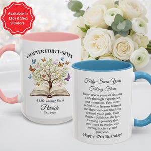 May include: Two white ceramic mugs with colorful accents. One mug has a pink handle and interior, featuring a tree design with butterflies and the text "Chapter Forty-Seven." The other mug has a blue handle and interior, with text about a 47th birthday.