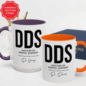 May include: Two white ceramic mugs with black text reading DDS DOCTOR OF DENTAL SURGERY creating smiles every day. One mug features a purple handle and interior, personalised with Dr. Nancy. The other has an orange handle and interior, personalised with Dr. Daniel. A red starburst graphic notes availability in 11oz and 15oz sizes and 9 colours.
