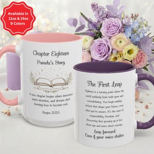 May include: Two white ceramic mugs with inspirational text and floral designs. One mug has a pink interior and handle, the other has a purple interior and handle. The mugs are surrounded by a bouquet of flowers.
