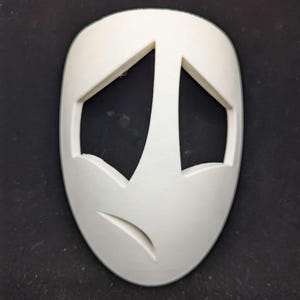 May include: A white, oval-shaped mask with cut-out eye and mouth shapes. The mask has a sad expression, with downward-sloping eye openings and a curved mouth. The mask is likely for costume or theatrical use.