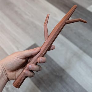 May include: A brown, 3D printed twig with a forked branch. The twig is made of a smooth, plastic-like material.