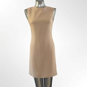 May include: A sleeveless, knee-length sheath dress in a solid light beige color. The garment features a high, round neckline and a straight, tailored silhouette that follows the natural lines of the torso, ending just above the knee.
