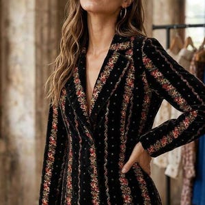 Peut inclure: Un blazer en velours noir orné de rayures verticales de broderies florales colorées et de sequins. La veste présente un revers cranté, des manches longues et une fermeture boutonnée. Le texte "Stule Monky" est visible en bas à gauche.