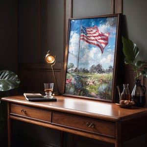 May include: A framed painting of the American flag waving in the wind, set against a blue sky with fluffy clouds. The artwork is displayed on a wooden desk with a lamp, a glass of amber liquid, and a small plant.