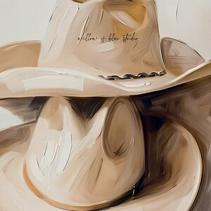 May include: Two beige cowboy hats stacked on top of each other. The top hat has the text "willow + blue studio" written on the crown.