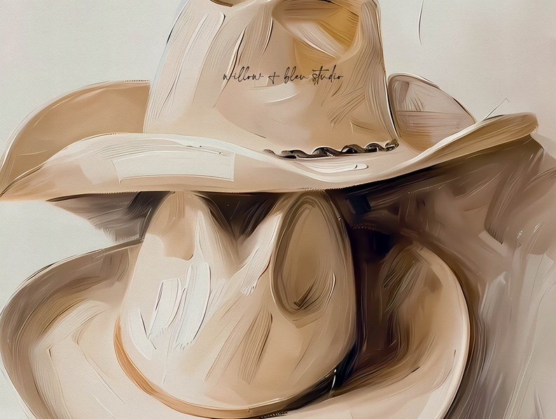 May include: Two beige cowboy hats stacked on top of each other. The top hat has the text "willow + blue studio" written on the crown.