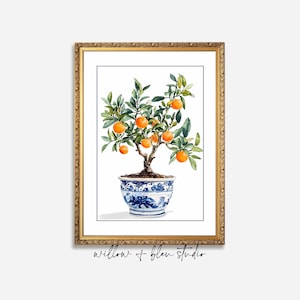 May include: Watercolor painting of a potted orange tree with ripe oranges and green leaves. The tree is in a blue and white patterned pot, framed in a gold ornate frame. The artwork is against a white background.