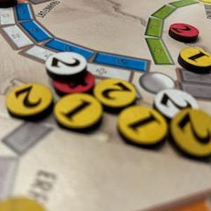 Könnte beinhalten: Nahaufnahme eines Spielbretts mit gelben, roten und weißen Spielsteinen. Die Spielsteine sind mit 1 und 2 nummeriert. Das Brett hat einen hellbraunen Hintergrund mit einem grünen und blauen Pfad.