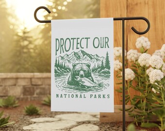 May include: White garden flag with a green illustration of a bear holding a fish in a lake with mountains and trees in the background. The text "PROTECT OUR NATIONAL PARKS" is printed on the flag.