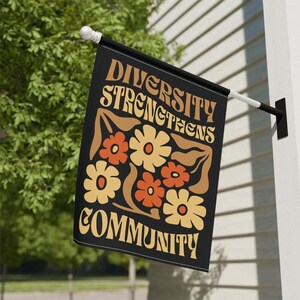 May include: A black flag with the text "Diversity Strengthens Community" in a retro font. The text is surrounded by a design of stylized flowers in orange, yellow, and brown.