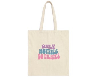 Può includere: Una borsa tote in tela bianca con il testo "ONLY HOTTIES DO PILATES" in lettere rosa, blu e viola.