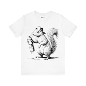 May include: White t-shirt with a black and white illustration of a squirrel wearing a baseball cap and holding a spray paint can.