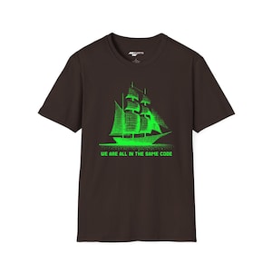 Peut inclure: Un t-shirt marron foncé avec un graphique vert d'un navire fait de code. Le texte "We are all in the same code" est imprimé sous le navire.