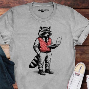 May include: Grey t-shirt with a cartoon raccoon wearing glasses, a red sweater vest, and holding a laptop. The raccoon is dressed in a suit and tie. The shirt has the text "MSHIRTS" on the upper left.
