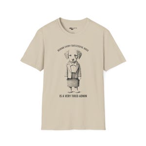 Op de afbeelding: Beige T-shirt met een zwart-witte illustratie van een hond die een pak en een rok draagt. De tekst "Behind every successful boss is a very tired admin" staat op het T-shirt gedrukt.