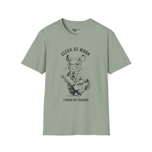 May include: Sage green t-shirt with a black and white illustration of a chinchilla wearing glasses and a suit holding a book. The text "Clerk at Work I know my folders" is printed on the shirt.