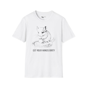 Puede incluir: Camiseta blanca con una ilustración en blanco y negro de un chinchilla usando un torno de alfarería. El texto "GET YOUR HANDS DIRTY" está impreso debajo de la ilustración.